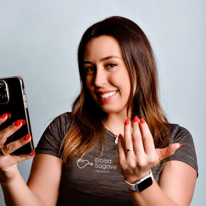 Eloisa Sagave sorrindo, com o celular na mão, num gesto de quem te chama para conversar.